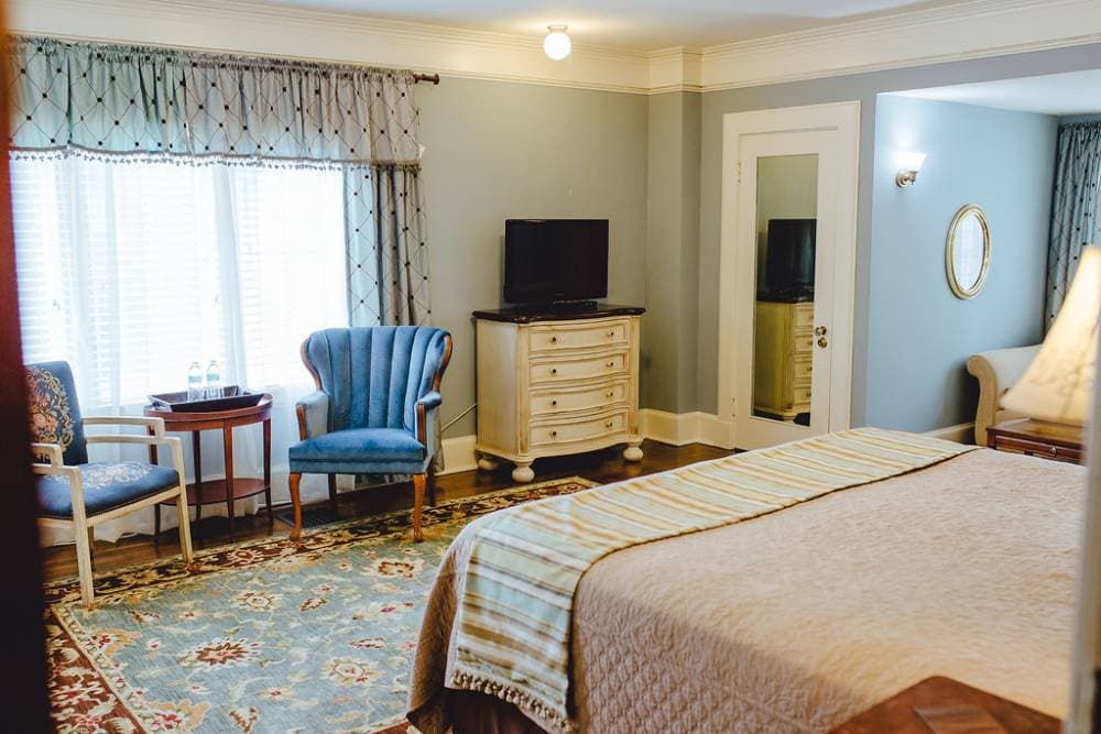 Sitting chairs are located opposite the bed in front of the large window.