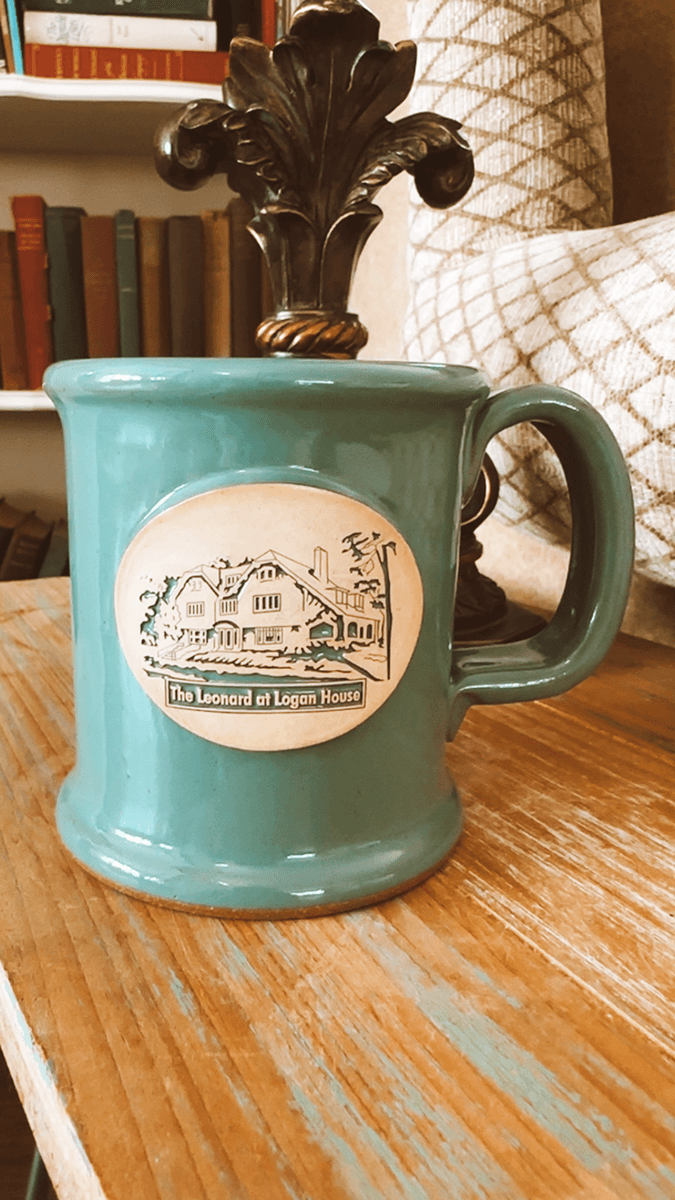 A vintage teal mug features an illustrated label of "The Leonard at Logan House."