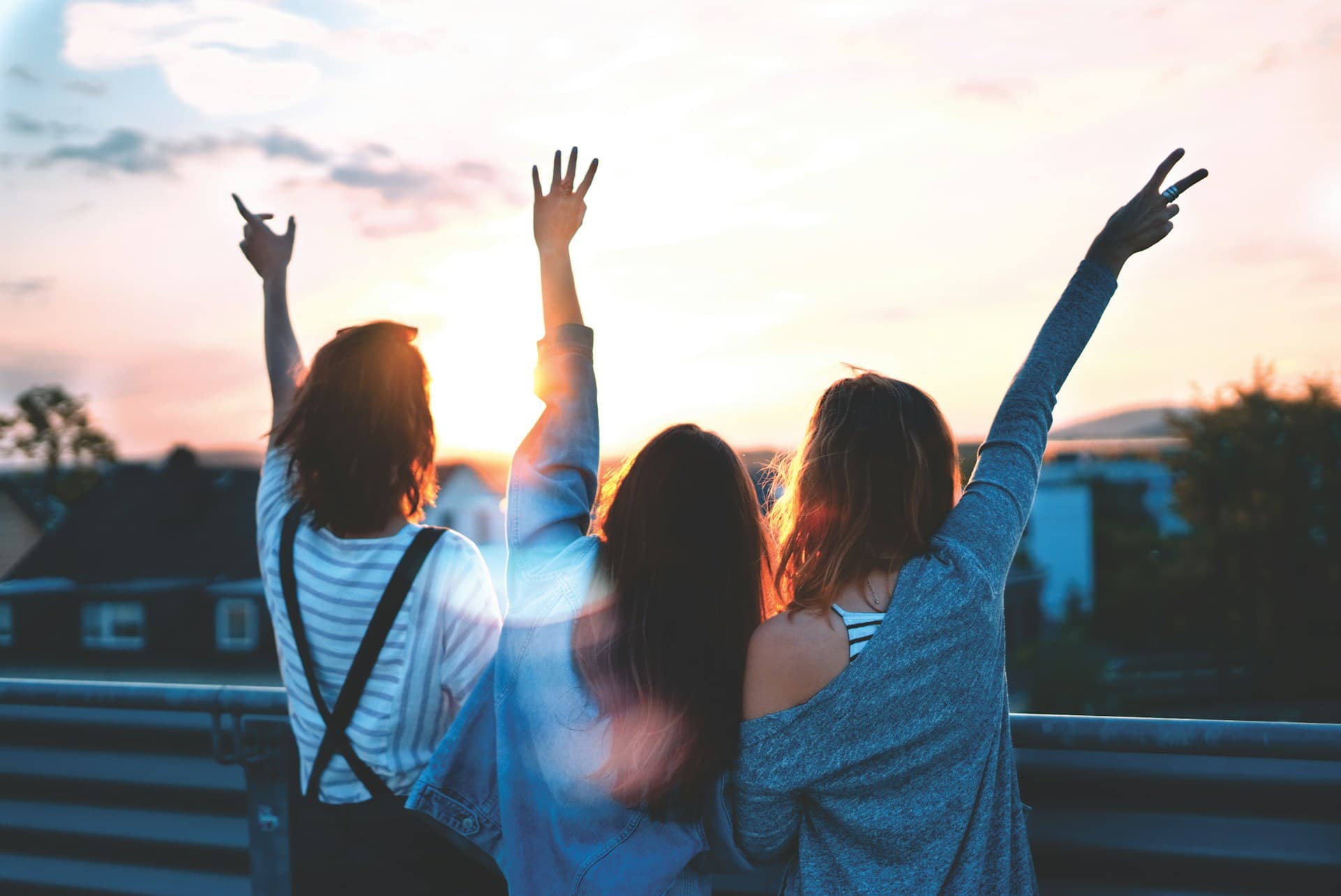 Three women raise their hands in celebration against a sunset backdrop.
