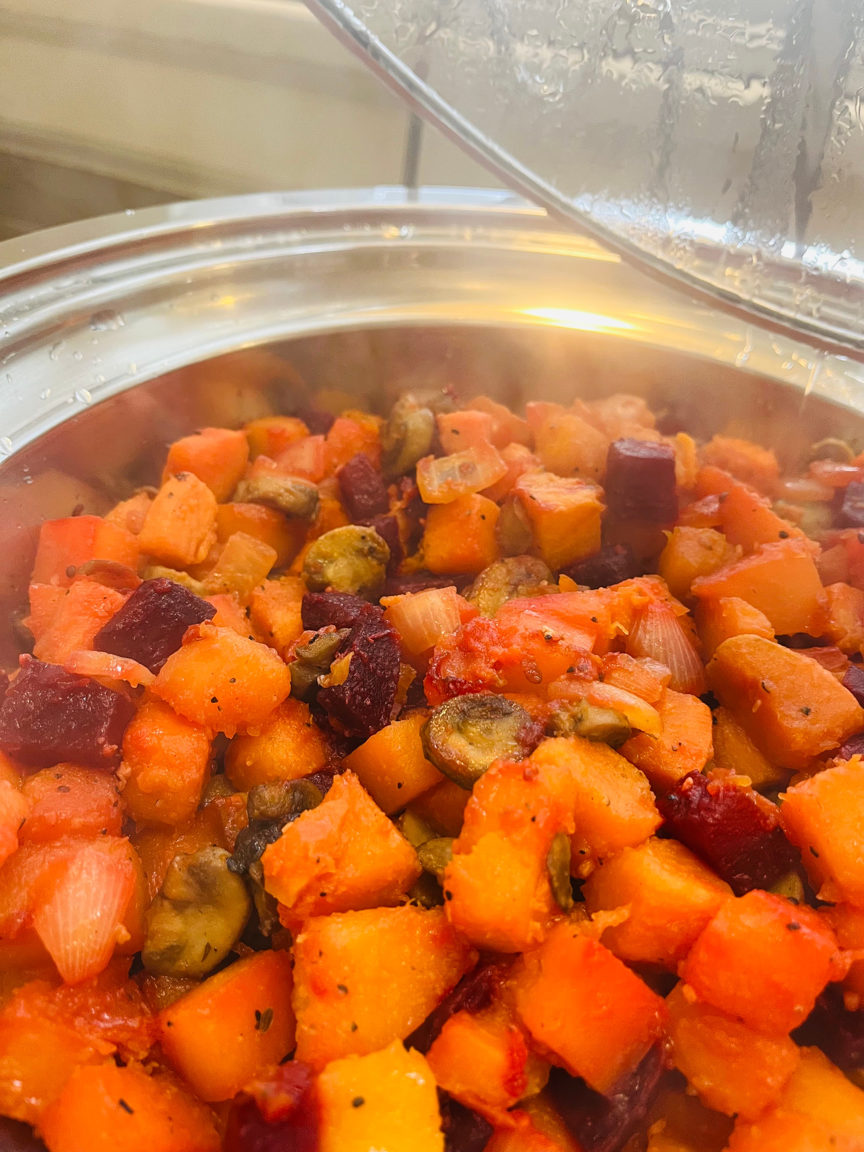 A steaming pot of colorful roasted vegetables, including squash, beets, and onions.