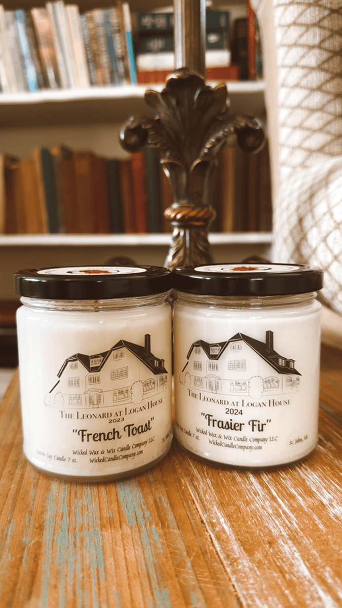 Two candle jars labeled "French Toast" and "Frasier Fir" on a wooden table with a bookshelf in the background.