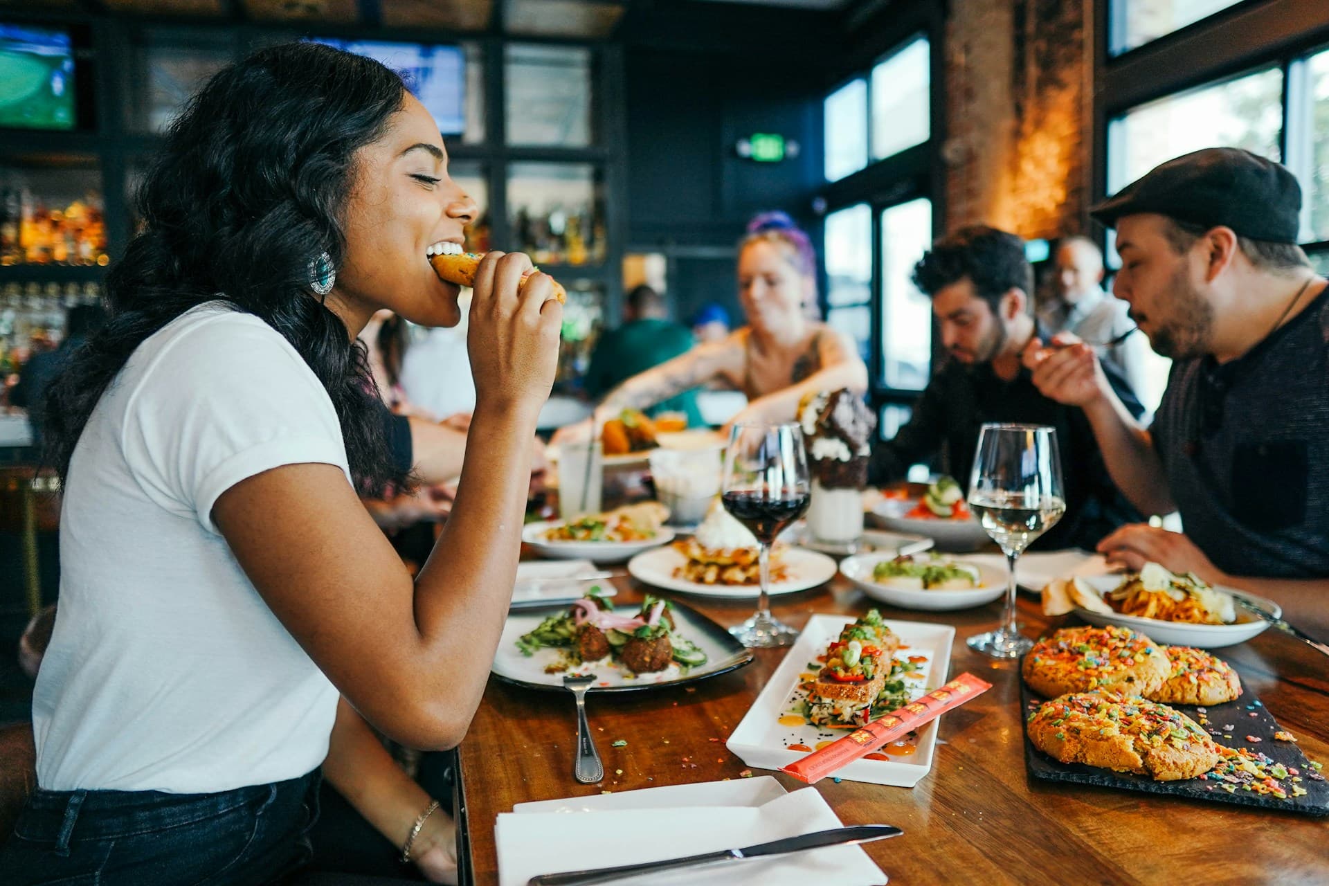 A group of friends enjoys a meal together at a bustling restaurant, featuring various plates of food and drinks.