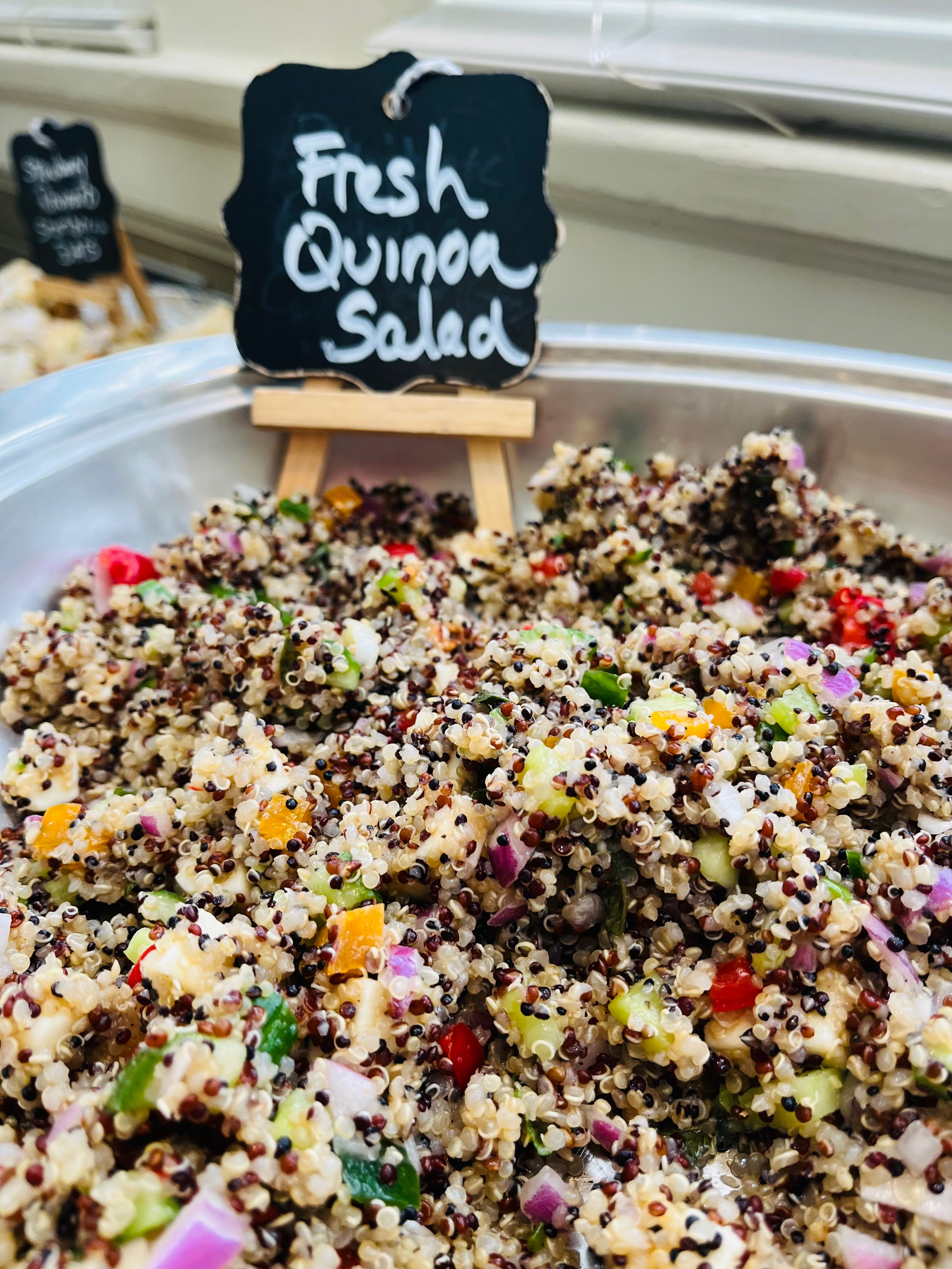 A bowl of fresh quinoa salad mixed with colorful vegetables, labeled on a small chalkboard.