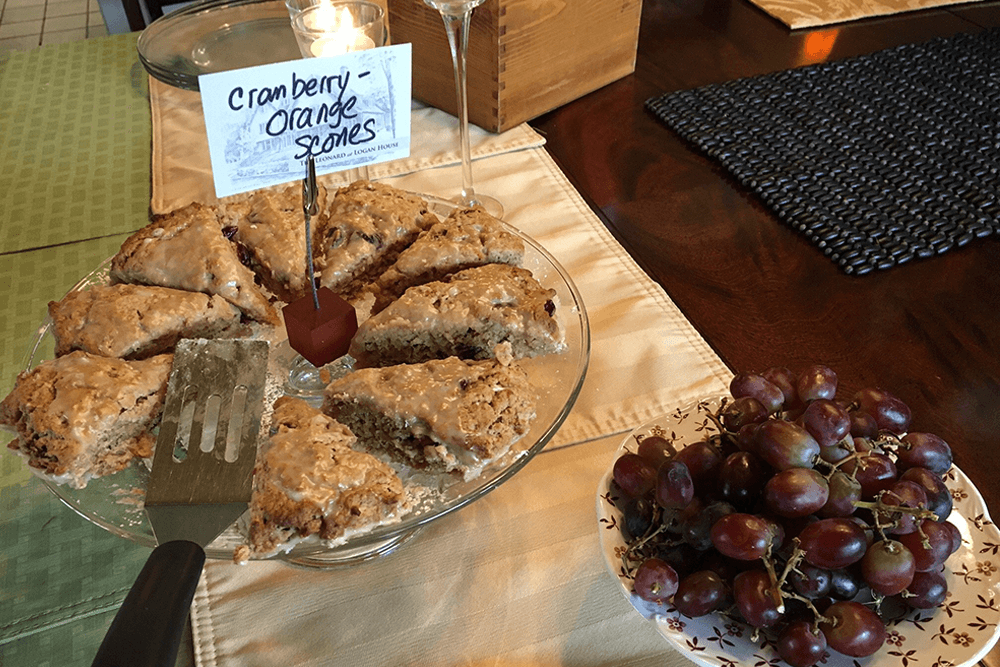 A plate of cranberry orange scones with a serving spatula and a bowl of grapes nearby.