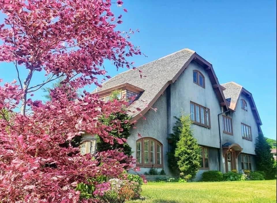A large house with a sloped roof surrounded by green lawn and pink flowering trees.