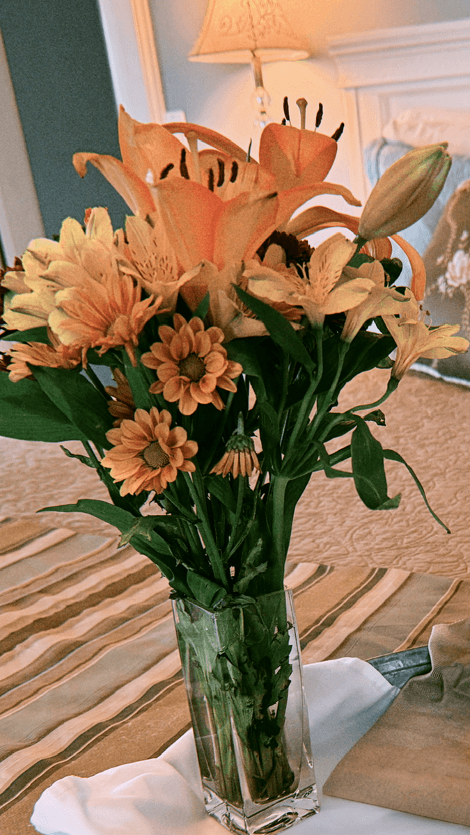 A vibrant bouquet of orange flowers in a clear vase on a patterned tablecloth.
