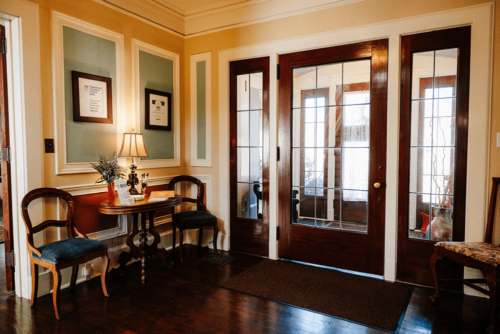 A cozy entryway with wood floors, a small table, two chairs, and large glass double doors.