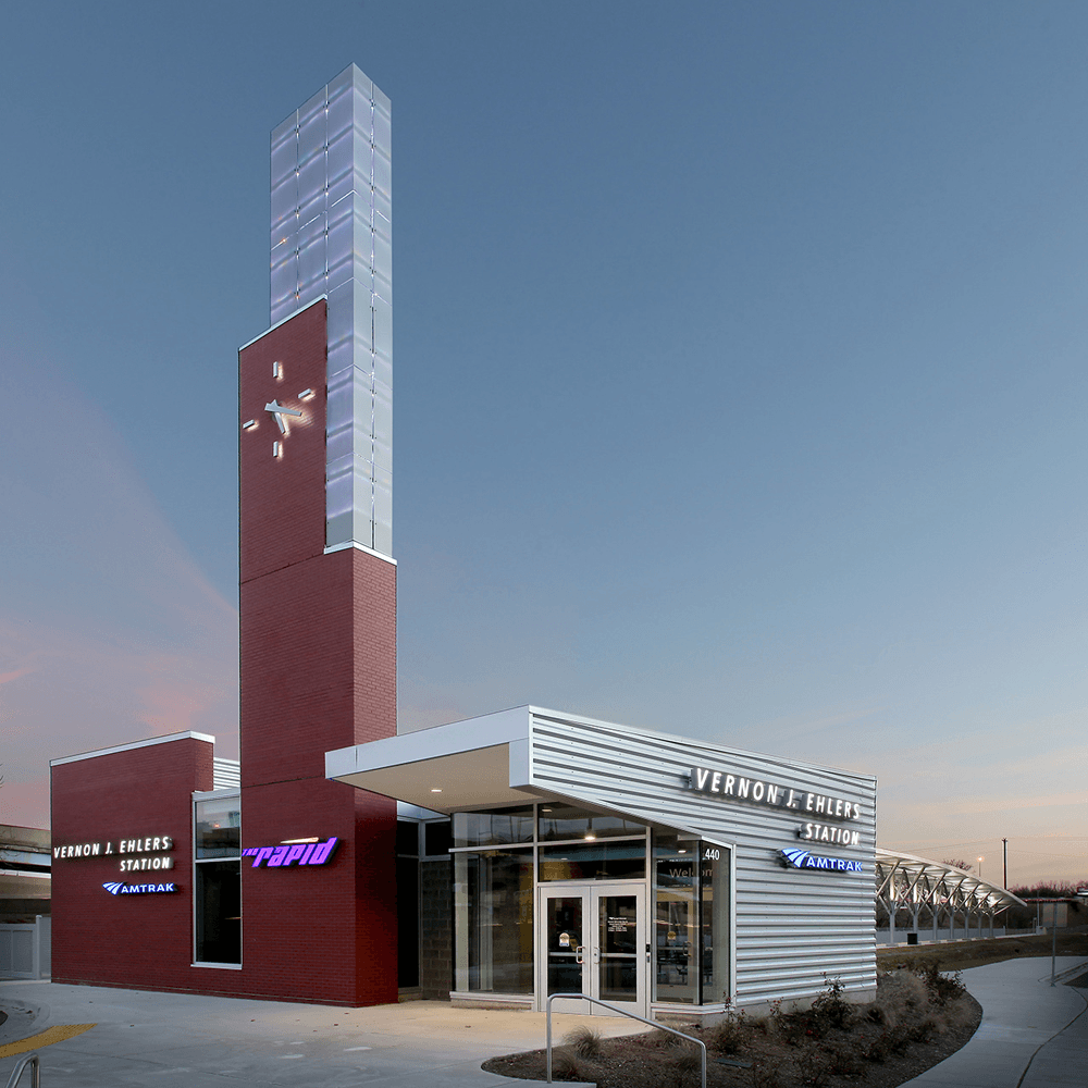 A modern train station with a tower clock and illuminated signage at dusk.