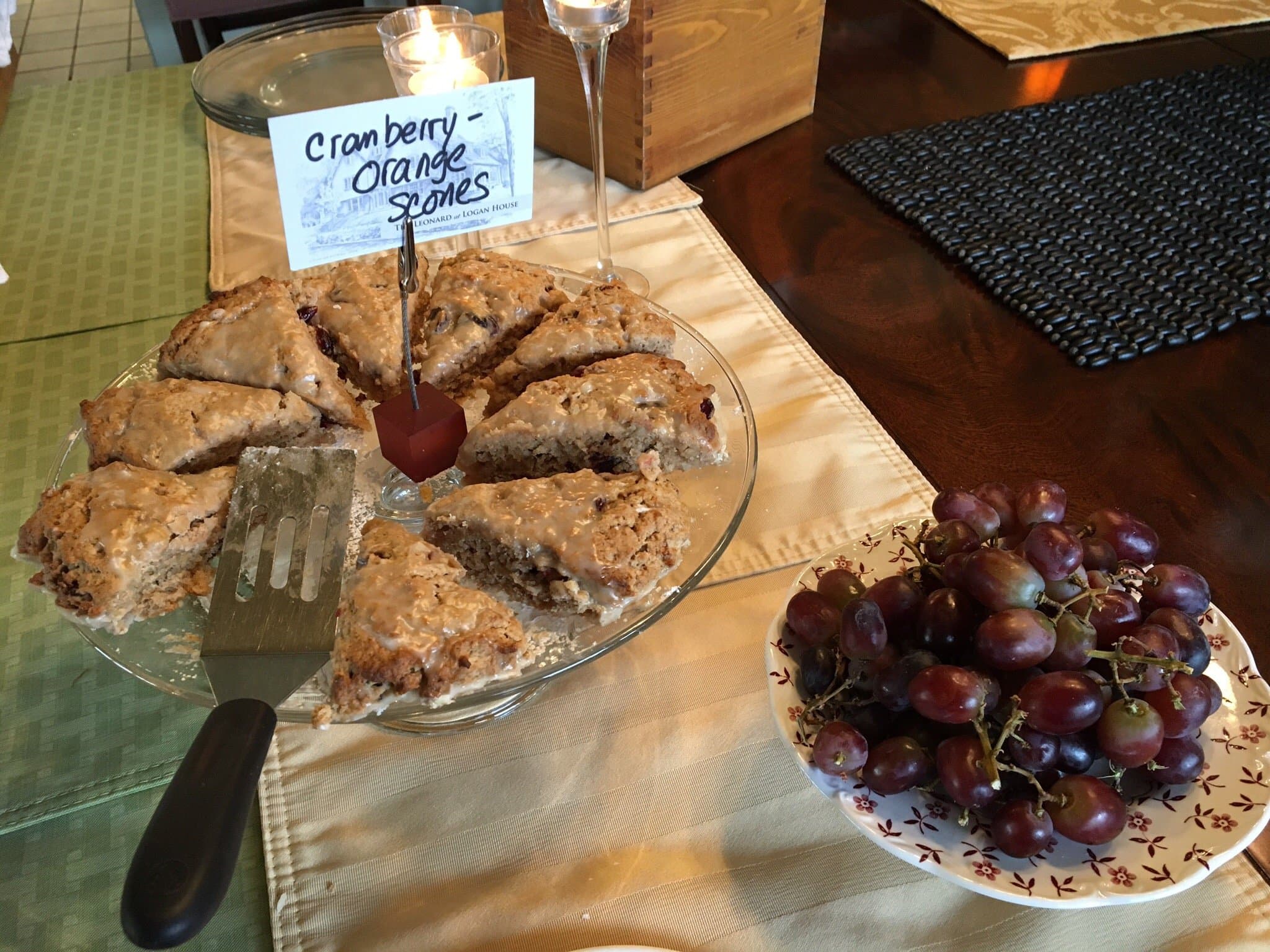 A plate of cranberry orange scones with a serving spatula, accompanied by a bowl of red grapes.