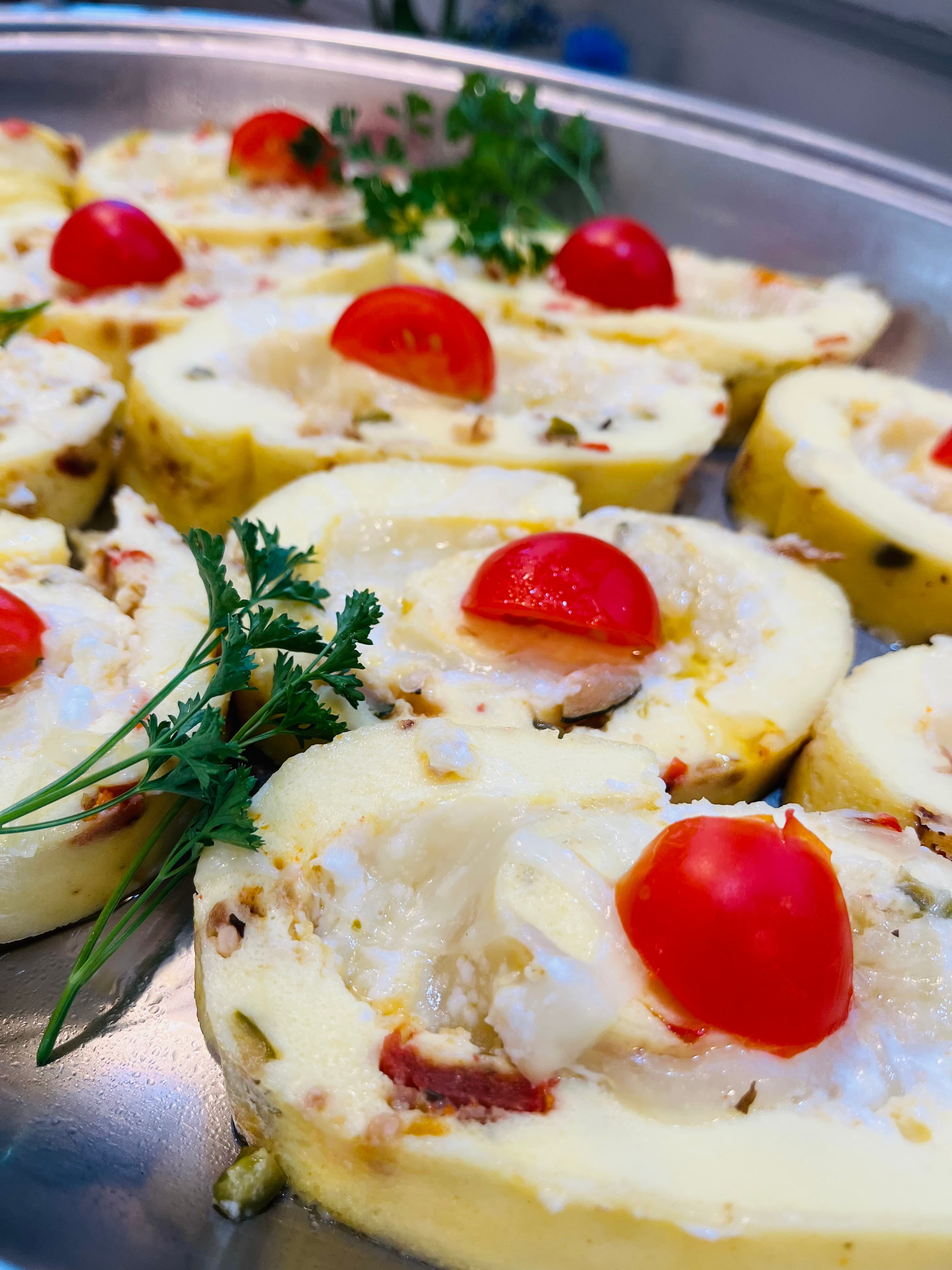 Sliced savory rolls filled with cheese, herbs, and topped with cherry tomatoes.