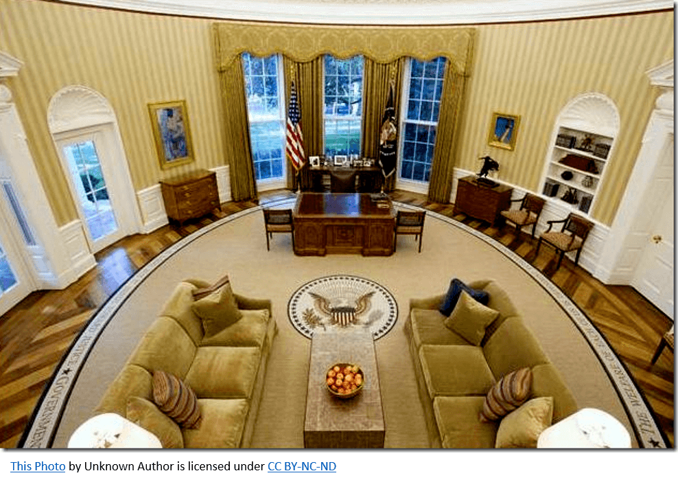 Aerial view of the Oval Office featuring a desk, sofas, and large windows.