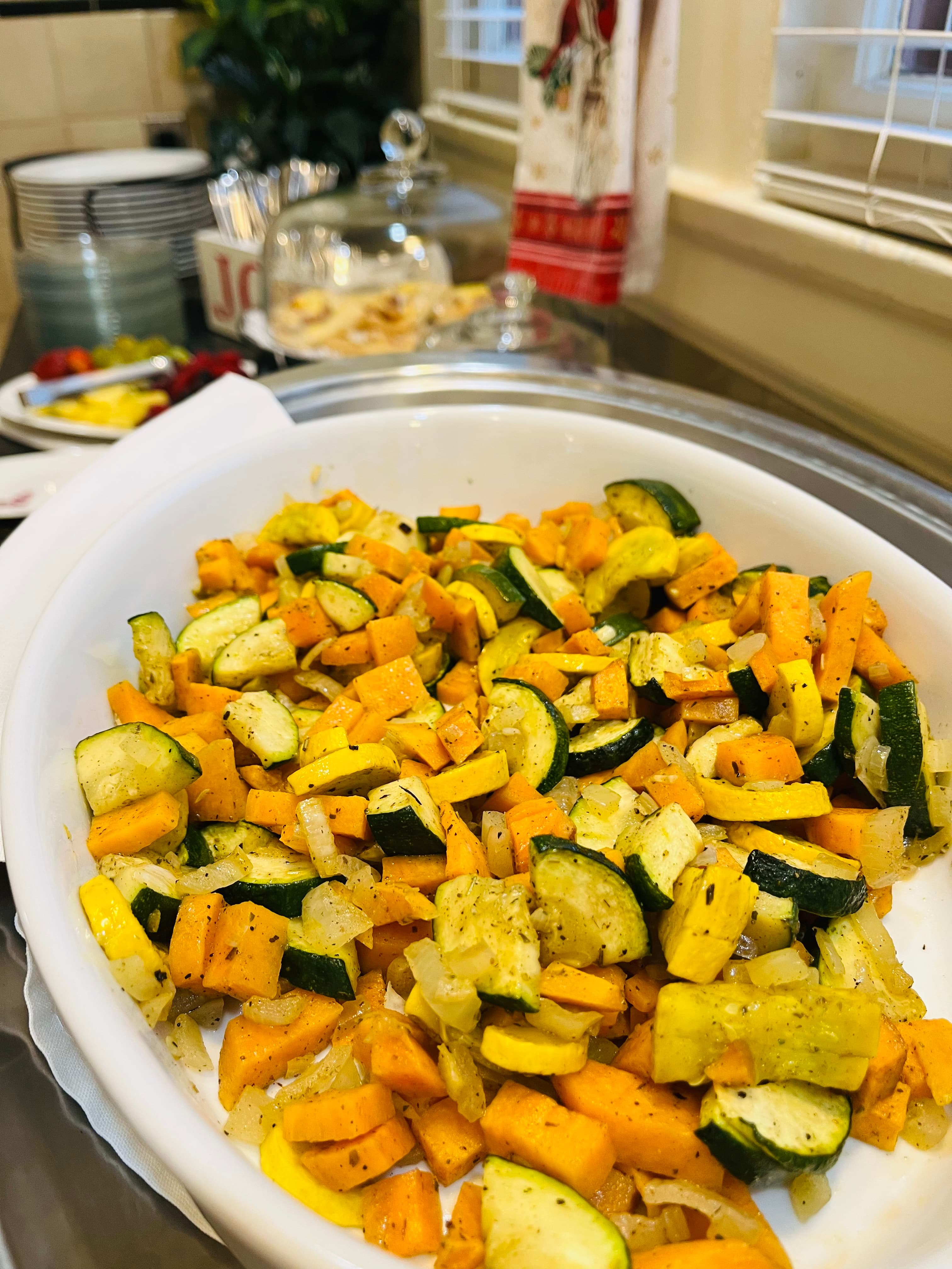 A white dish filled with sautéed yellow squash, zucchini, sweet potatoes, and onions.